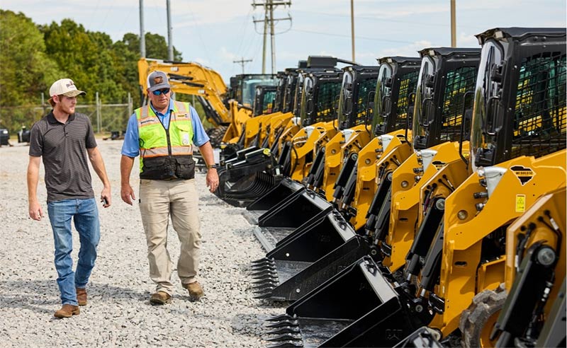 HOLT CAT team member walking a customer along a row of Cat skid steers